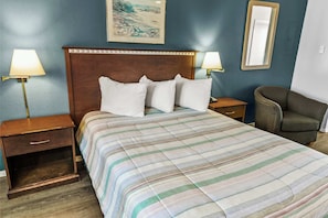 Habitació d'hotel amb llit, dues taules de nit, una cadira, un taulell de nit i un mirall fixat a la paret.