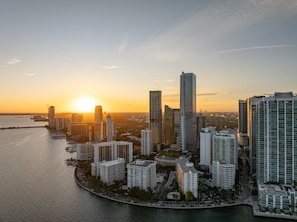 Et højt byområde med en havnefront, der viser moderne arkitektur og en solnedgang.