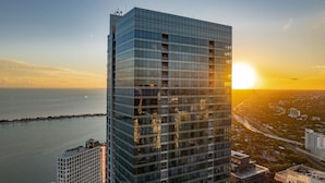 Un immeuble de grande hauteur doté d’une façade en verre, situé près d’une étendue d’eau, avec un coucher de soleil en arrière-plan.