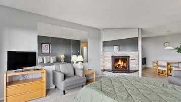 A modern hotel room with a flat-screen TV, a sofa, a fireplace, and a dining area.
