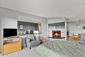 A modern hotel room with a flat-screen TV, a sofa, a fireplace, and a dining area.