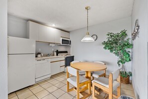 A compact kitchen with white cabinets, a microwave, a stove, and a dining table with chairs.