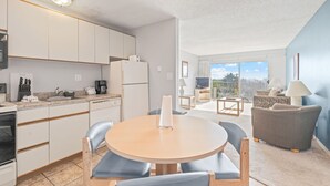 Une cuisine moderne avec des meubles blancs, une table à manger avec des chaises et un coin salon comprenant un canapé et un téléviseur.