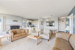 A living room with a sofa, armchairs, a coffee table, a fireplace, and a kitchen in the background.