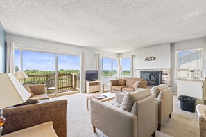 A spacious living room with a fireplace, large windows, and a balcony.