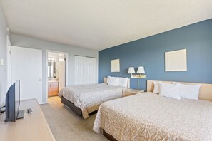 A hotel room with two beds, a desk with a television, a bathroom with a mirror, and a nightstand with lamps.