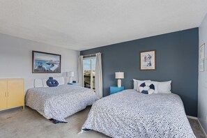 Une chambre d’hôtel avec deux lits, une fenêtre avec des rideaux, une armoire jaune et des œuvres d’art accrochées aux murs.