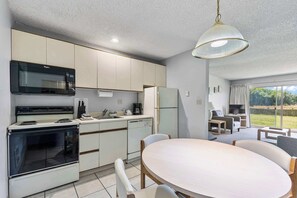 Une cuisine moderne équipée d’un four à micro-ondes, d’une cuisinière et d’un réfrigérateur, un coin repas avec une table et des chaises, et une grande fenêtre donnant sur l’extérieur.
