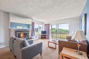 A living room with a fireplace, sofas, a TV, and a balcony with a view. - 2-Bedroom Family Suite With King Bed and Kitchen (Ocean Shores)