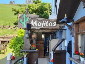 Um restaurante chamado 'Mojitos' com área externa, uma placa de madeira e vista para uma colina verde.