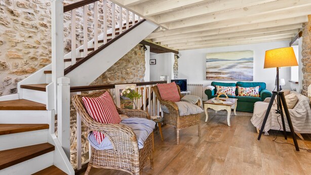 A cozy living room with a stone wall, wooden staircase, wicker furniture, and a painting on the wall.