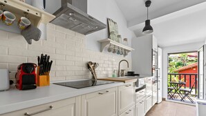 A modern kitchen with white cabinetry, a stainless steel sink, and a built-in oven. There is a window with a view of a red building and greenery outside.