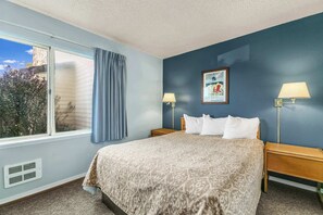 A bedroom with a large bed, two bedside lamps, a window with a view, and a wall-mounted picture. - Pet-Friendly 2-Bedroom Family Suite With Fireplace (Ocean Shores)