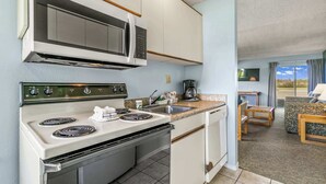 A compact kitchen with a microwave, stove, and sink. There is a dining area with a table and chairs. - Pet-Friendly 2-Bedroom Family Suite With Fireplace (Ocean Shores)