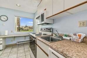 Una cocina con ventana, estufa, microondas, lavaplatos y encimera.