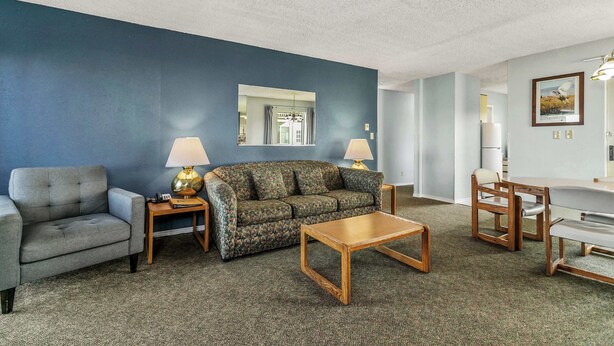 A living room with a blue wall, a grey sofa, a floral sofa, a wooden coffee table, and a dining area with a white table and wooden chairs. - Pet-Friendly 2-Bedroom Family Suite With Fireplace (Ocean Shores)