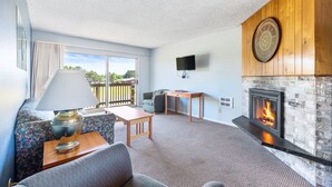 A living room with a fireplace, sofa, table, lamp, and a TV mounted on the wall. - Pet-Friendly Suite For 6 - Pool & Hot Tub Access! (Ocean Shores)