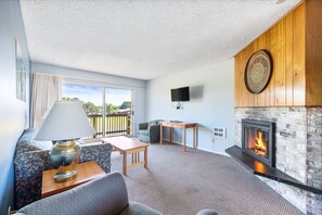 Una sala de estar con chimenea, sofá, mesa, lámpara y televisor montado en la pared.