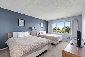 Ein Hotelzimmer mit zwei Betten, einem Schreibtisch mit Computer, einem Fenster mit Blick auf Grünflächen und einem Deckenventilator.