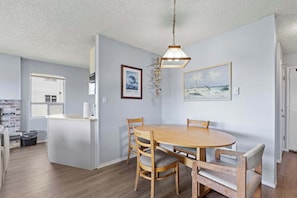 A dining area with a round wooden table and chairs, a hanging light fixture, and wall-mounted artwork. - Pet-Friendly Family Fireplace Suite - Kitchen - Pool and Hot Tub! (Ocean Shores)