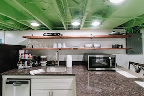 Una cocina con encimeras de granito, microondas, fregadero y estantes de madera.