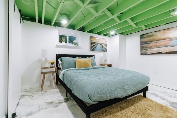 Un dormitorio con cama, mesitas de noche, techo verde y obras de arte en las paredes.
