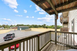 A wooden deck with a view of a parking lot and a building with a balcony. - Pet-Friendly One-Bedroom Condo - Pool & Hot Tub! (Ocean Shores)