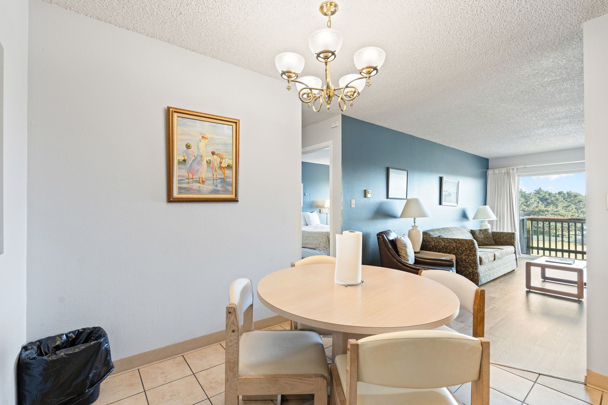 A dining area with a round table, chairs, a chandelier, and a painting on the wall.