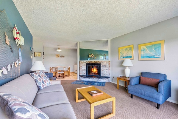 A living room with a fireplace, a sofa, a blue armchair, and a coffee table. - Ground Floor Pet Friendly Suite - Kitchen & Patio (Ocean Shores)