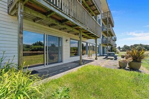 Ein modernes, zweistöckiges Haus mit überdachter Terrasse, großen Schiebeglastüren und einer kleinen Sitzgelegenheit im Freien.