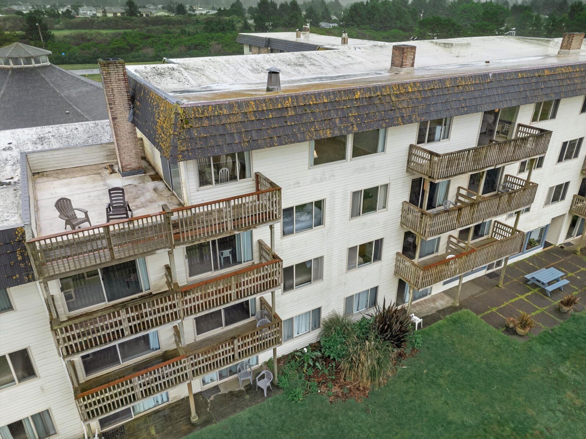 Un immeuble résidentiel à plusieurs étages, doté de balcons, d’un toit plat et d’un petit espace jardin.