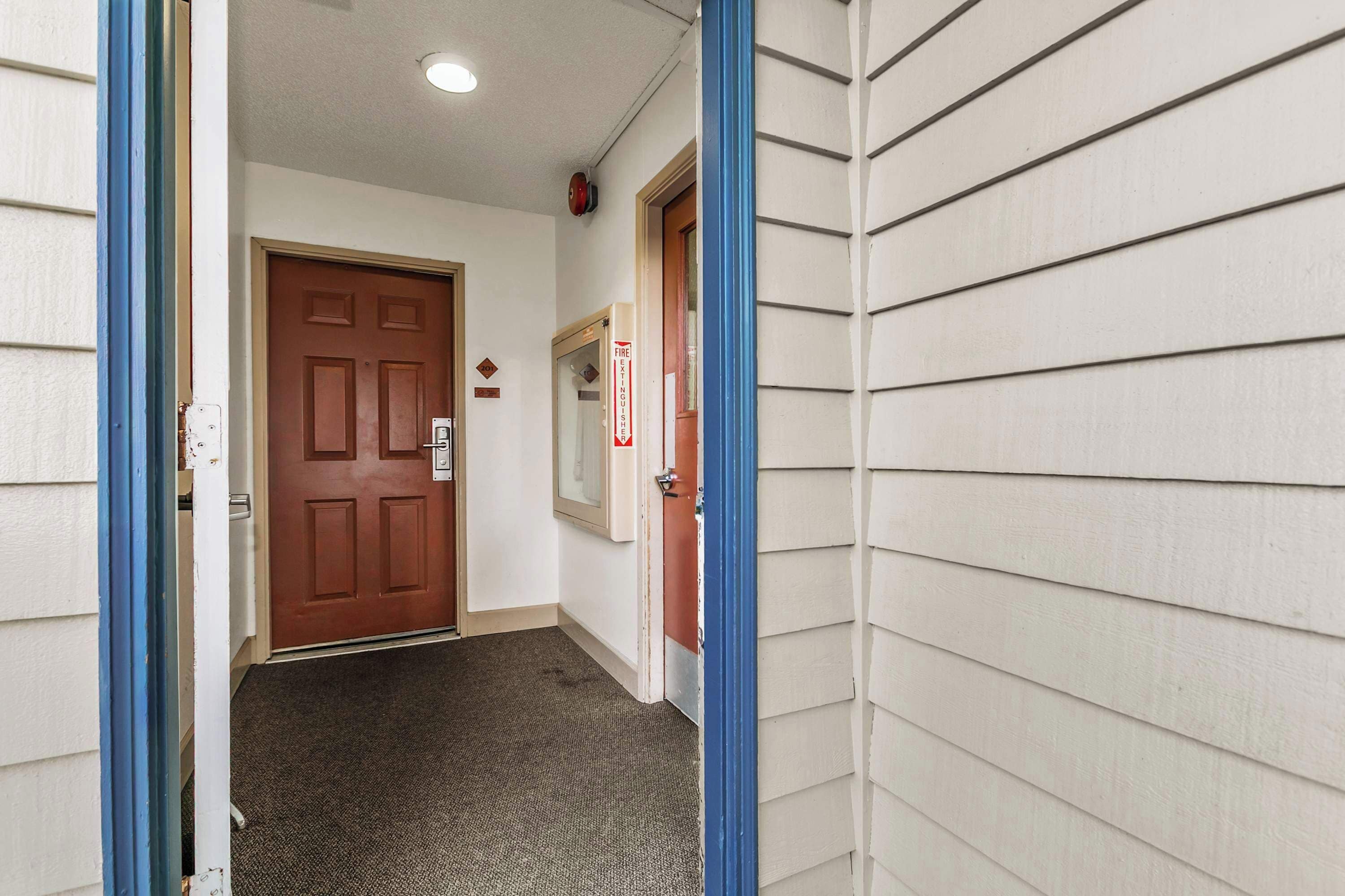 A hallway with a brown door, a fire alarm, and a blue door frame.