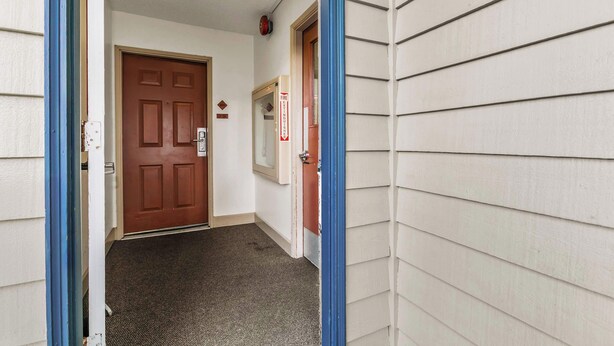 A hallway with a brown door, a fire alarm, and a blue door frame. - 2-Bedroom Condo - King Bed, Fireplace, & Kitchen! (Ocean Shores)