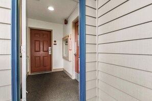 En hall med en brun dörr, en brandlarm och ett blått dörrfoder.