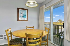 Un comedor con una mesa redonda de madera y cuatro sillas, un cuadro en la pared, y vistas al exterior a través de una puerta de cristal.