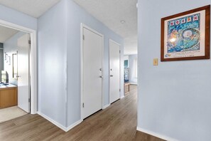 Ein Korridor mit hellblauen Wänden, Holzboden, weißen Türen und einem gerahmten Poster an der Wand.