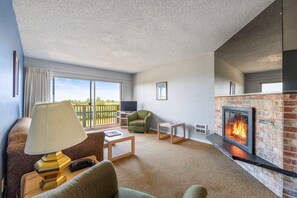 A living room with a fireplace, a sofa, a television, and a view of the outdoors. - Ocean View, Pet-Friendly 1-Bedroom Family Suite - Pool and Hot Tub! (Ocean Shores)