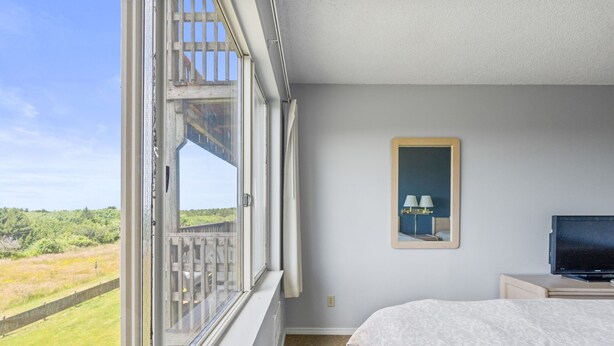 A bedroom with a large window, a bed, a television, and a framed picture on the wall. - Ocean View, Pet-Friendly 1-Bedroom Family Suite - Pool and Hot Tub! (Ocean Shores)