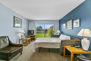Une chambre d’hôtel avec un lit, un canapé, une télévision, une table et une vue sur un paysage verdoyant.