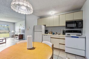 A modern kitchen with white cabinets, a microwave, a stove, and a dining area with a wooden table and chairs.
