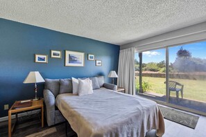 Ein Schlafzimmer mit einem Bett, zwei Nachttischen, einem Fenster mit Blick ins Freie und gerahmten Bildern an der Wand.