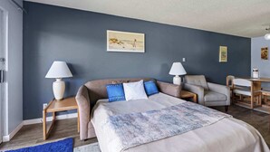 A bedroom with a bed, two bedside tables, a chair, a desk, and a painting on the wall. - Pet Friendly Suite with Patio - Pool and Hot Tub! (Ocean Shores)