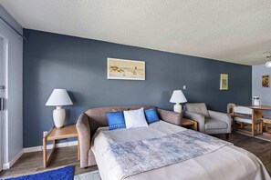 Ein Schlafzimmer mit einem Bett, zwei Nachttischen, einem Sessel, einem Schreibtisch und einem Bild an der Wand.
