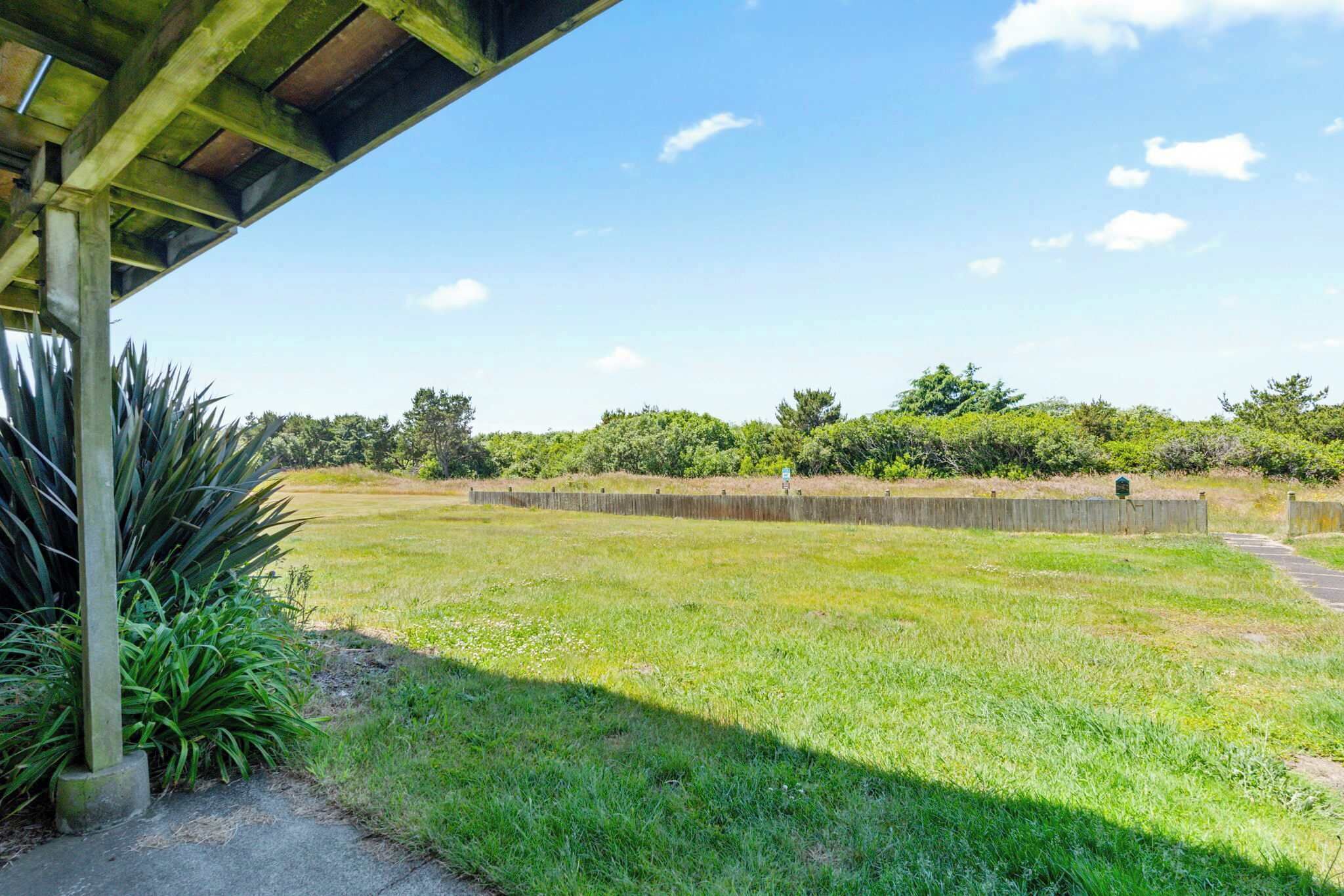 A grassy area with a wooden structure, a concrete wall, and a pathway leading to a green sign.