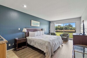 Ein Schlafzimmer mit Bett, Nachttisch, Lampe, Stuhl, Schreibtisch und Blick ins Freie.