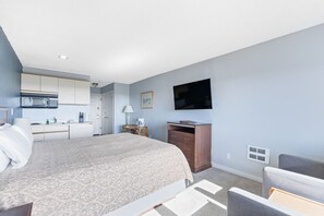 A hotel room with a bed, a desk with a microwave, a television, and a small cabinet. - King Bed, Ocean View Studio with Pool and Hot Tub! (Ocean Shores)