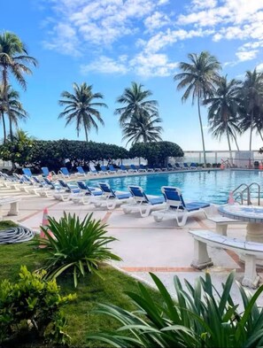 A pool area with lounge chairs, palm trees, and a clear sky. - Corner For 2 BEAUTIFUL OCEAN VIEW Pool Beach Parking CONDADO (San Juan)