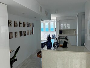 A modern kitchen with a central island, a dining area with a view, and a hallway with artwork. - Corner For 2 BEAUTIFUL OCEAN VIEW Pool Beach Parking CONDADO (San Juan)