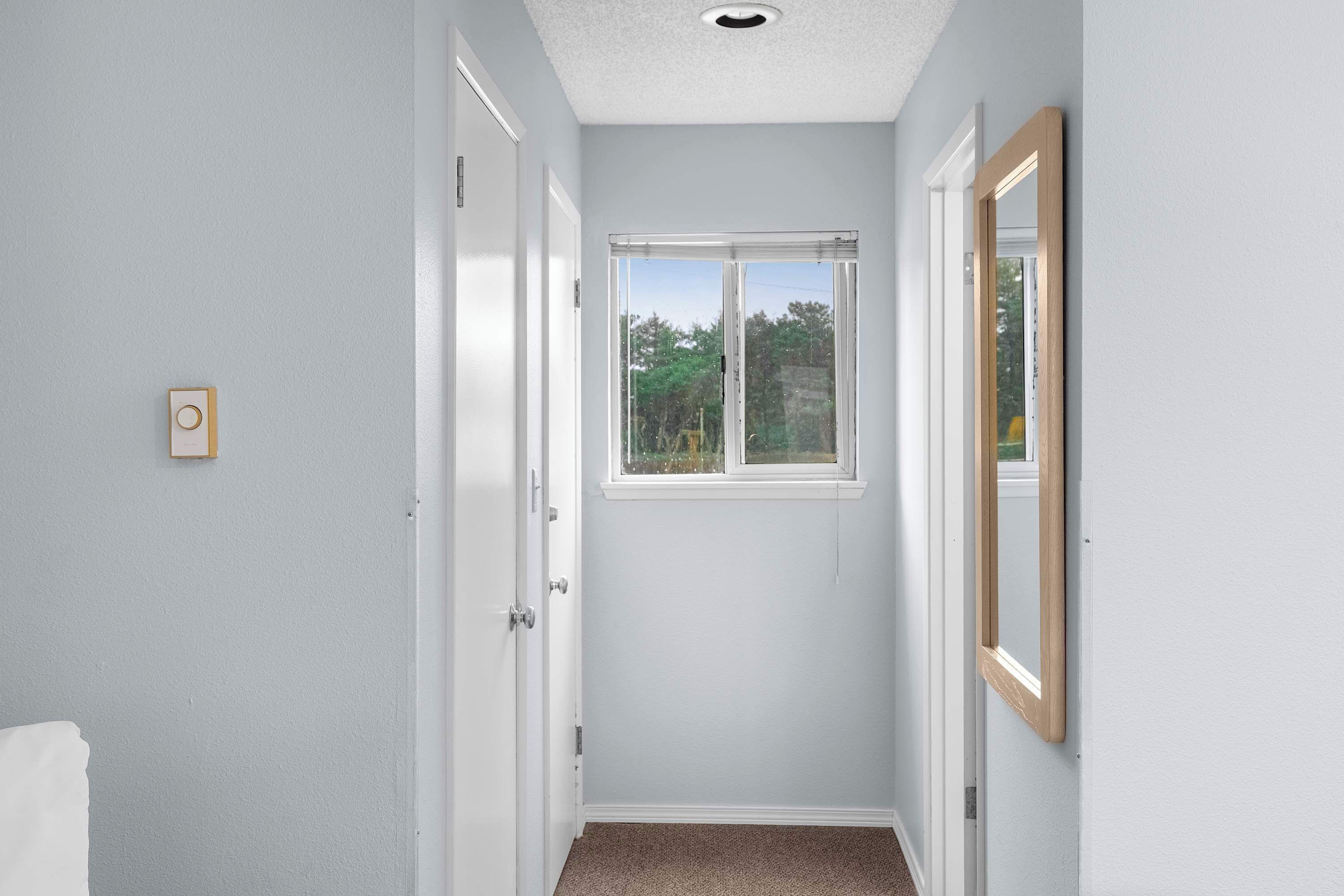Un couloir étroit avec une fenêtre, une porte et un miroir au mur.