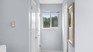 Un couloir étroit avec une fenêtre, une porte et un miroir au mur.